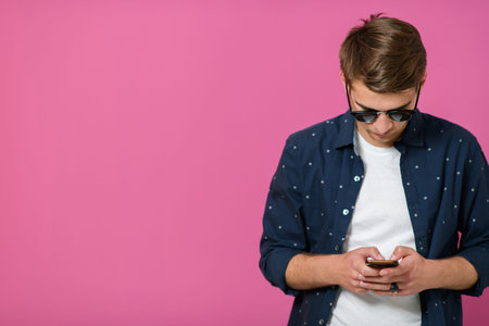 a young man wearing a blue shirt and sunglasses using a smartphoneの写真素材