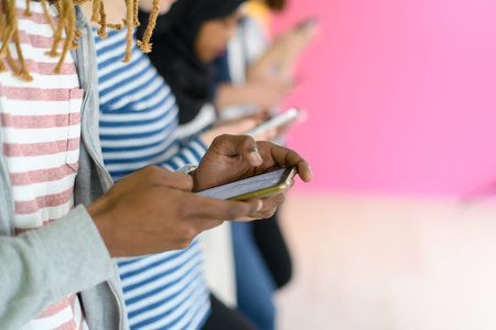 diverse teenagers use mobile devices while posing for a studio photo in front of a pink background
