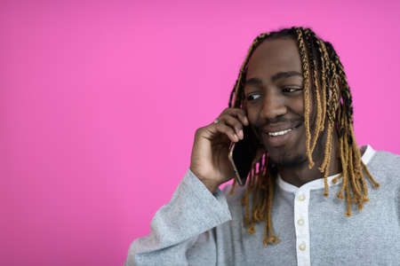 afro guy uses a phone while posing in front of a pink background.の写真素材