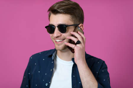 a young man wearing a blue shirt and sunglasses using a smartphoneの写真素材