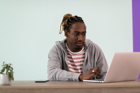 an afro young man sits in his home office during a pandemic and uses laptopの写真素材