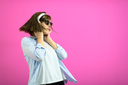 brunette lady in black glasses dancing and listening music isolate on pink background