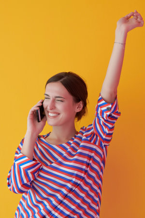 Portrait of young girl talking on the phone while standing in front of yellow backgroundの写真素材