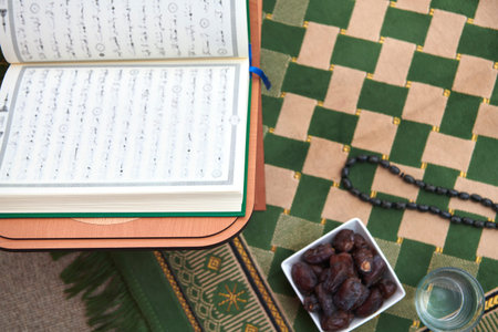 Iftar time dried dates holy Quran glass of water and tasbih on praying rug or sejadah