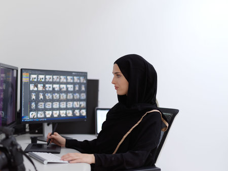 Muslim female graphic designer working on computer using graphic tablet and two monitors
