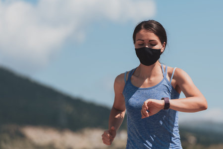 Determined fitness woman in short clothes wearing red protective face mask running outdoors in the...