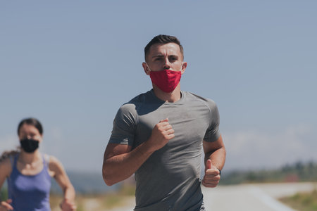 Young man and woman in protective masks running and doing exercises outdoors in the morning. Sport, Active life Jogging during quarantine. Covid-19 new normal. Selective focus.の写真素材
