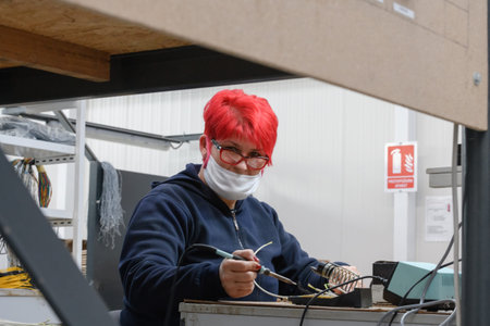 Industrial worker wearing a face mask due to a coronavirus pandemic solders cables from factory production equipmentの写真素材