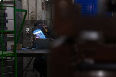 Professional welder performs work with metal parts in factory, sparks and electricity. Industry...
