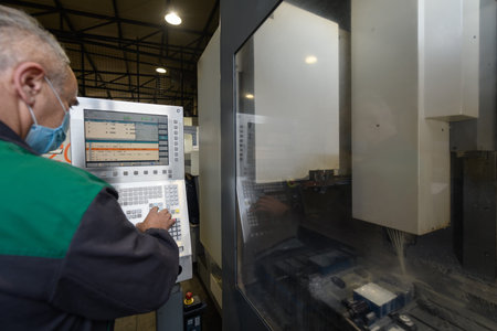A smart factory worker or engineer wears a face mask because of a pandemic and makes machines in a...
