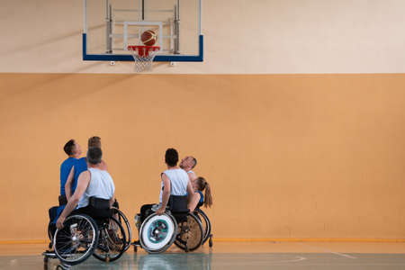 Disabled War veterans mixed race opposing basketball teams in wheelchairs photographed in action while playing an important match in a modern hall.の写真素材