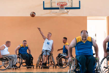 Disabled War veterans mixed race and age basketball teams in wheelchairs playing a training match in a sports gym hall. Handicapped people rehabilitation and inclusion conceptの写真素材
