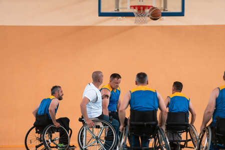 Disabled War veterans mixed race and age basketball teams in wheelchairs playing a training match in a sports gym hall. Handicapped people rehabilitation and inclusion conceptの写真素材