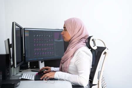 Female Arabic creative professional working at home office on desktop computer with dual screen monitor top view. Selectve focusの写真素材