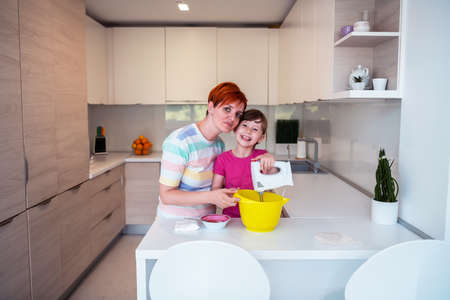 Funny little girl helper playing with dough on his hands learning to knead helps adult mom in the kitchen, happy cute baby daughter and parent mom have fun cooking cookies.の写真素材