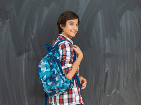 arab teenager with backpack wearing casual school look against black chalkboard backgroundの写真素材