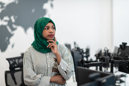 Portrait of muslim black female software developer with green hijab standing at modern open plan...