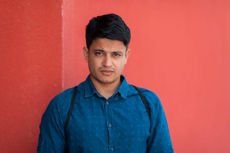 Startup business portrait of casual businessman with a blue shirt and backpack in front of red wall