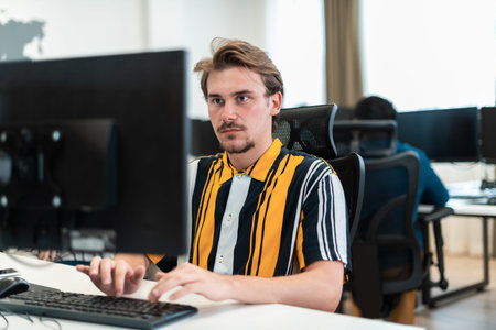 Casual man working on desktop computer in modern open plan startup office interior. Selective focus
