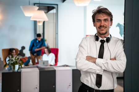 Portrait of successful businessman entrepreneur with headphones around his neck and colleagues in the background at busy startup officeの写真素材