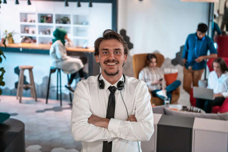 Portrait of successful businessman entrepreneur with headphones around his neck and colleagues in the background at busy startup officeの写真素材