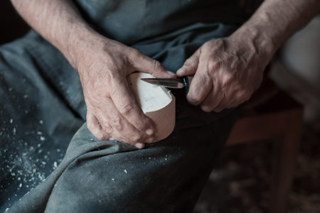 Hands carving cup from wood, working with chisel close up. Wooden workshop. Process of making wooden...