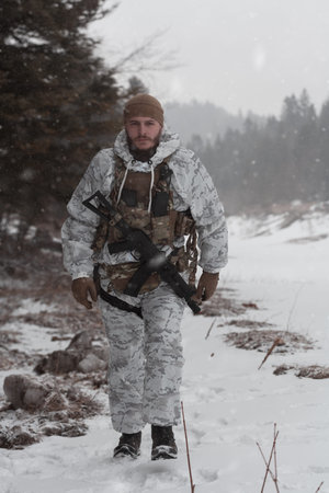 Soldier in winter camouflaged uniform in Modern warfare army on a snow day on forest battlefield...