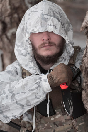 Soldier in winter camouflaged uniform in Modern warfare army on a snow day on forest battlefield...