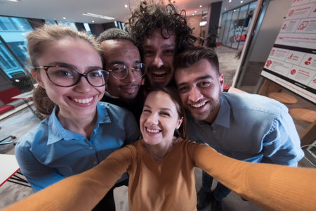 Group of business people during break from the work taking selfie picture while enjoying free time in relaxation area at modern open plan startup office. Selective focusの写真素材