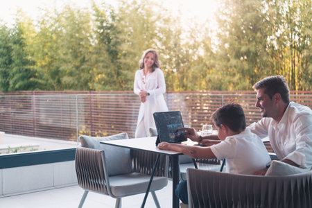 A happy elderly couple resting on the balcony of a luxury house, father and son using a tablet. Selective focusの写真素材