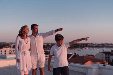 Happy family enjoys and spends time together on the roof of the house while watching the sunset on the open sea togetherの写真素材