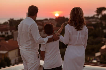 Happy family enjoys and spends time together on the roof of the house while watching the sunset on the open sea togetherの写真素材