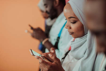 A group of African Muslim students use smartphones while standing in front of a yellow backgroundの写真素材