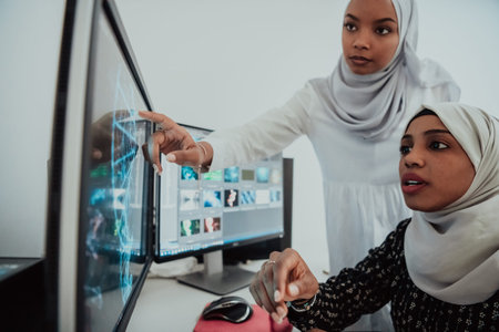 Friends at the office two young Afro American modern Muslim businesswomen wearing scarf in creative...