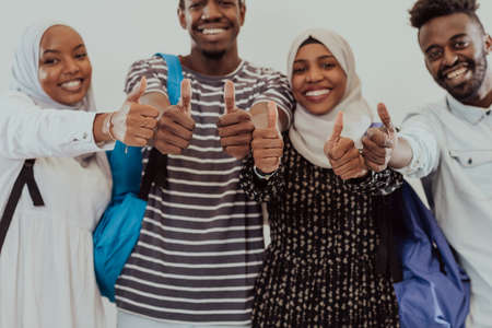 Group portrait of happy African students standing together against a white background and showing ok sign thumbs up girls wearing traditional Sudan Muslim hijab fashionの写真素材