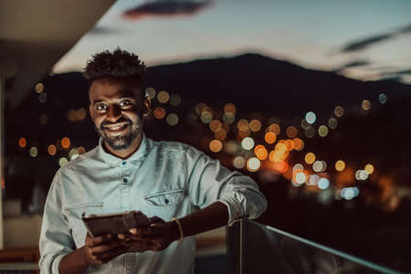 The young man on an urban city street at night texting on smartphone with bokeh and neon city lights in the background.の写真素材