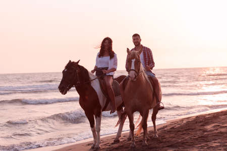 a loving couple in summer clothes riding a horse on a sandy beach at sunset. Sea and sunset in the background. Selective focusの写真素材