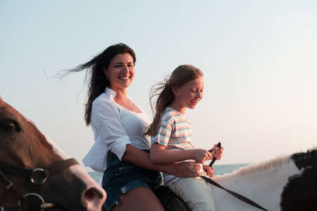 Mother and daughter enjoy riding horses together by the sea. Selective focusの写真素材