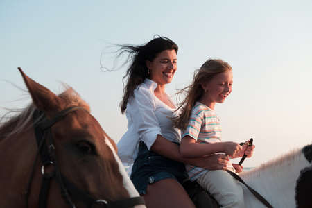 Mother and daughter enjoy riding horses together by the sea. Selective focusの写真素材