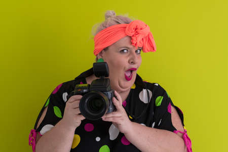 plus size smiling woman with funny emotional face expression with vintage camera in dress isolated on green background, traveler on vacation, summer fashion style, excited tourist.の写真素材