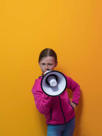 Funny little kid girl Screaming in megaphone over the yellow background in studio. People sincere emotions lifestyle concept.の写真素材