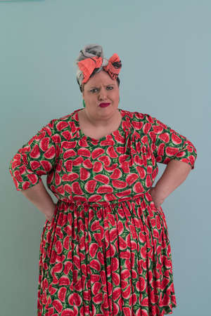 Plus size sexy model woman with trendy makeup, fashionable blonde in colorful dress posing at the cyan or light blue background in studio.の写真素材