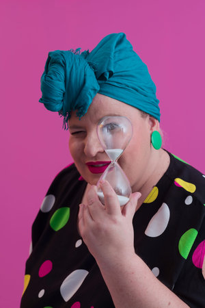 Portrait of plus size young lady smiling hands holds sand clock isolated on pink color background.