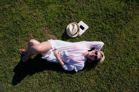 Top view from above of a woman lying and relaxing on a meadow covered with green grass on a sunny...