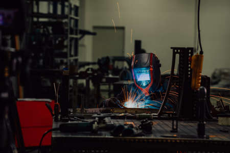 Professional Heavy Industry Welder Working Inside factory, Wears Helmet and Starts Welding. Selective Focusの写真素材