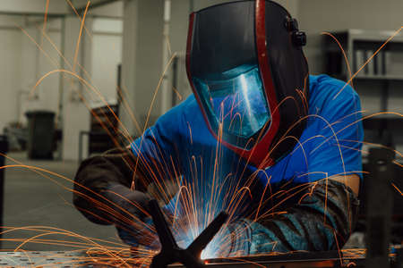 Professional Heavy Industry Welder Working Inside factory, Wears Helmet and Starts Welding. Selective Focusの写真素材