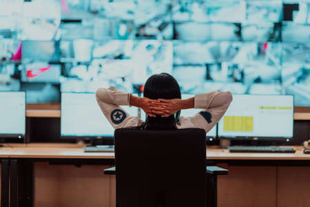 Female security operator working in a data system control room offices Technical Operator Working at workstation with multiple displays, security guard working on multiple monitorsの写真素材