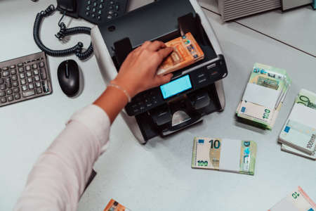 Bank employees using money counting machine while sorting and counting paper banknotes inside bank vault. Large amounts of money in the bankの写真素材