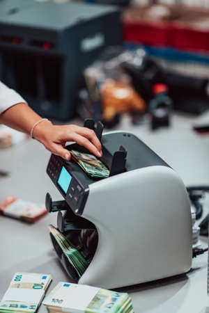 Bank employees using money counting machine while sorting and counting paper banknotes inside bank vault. Large amounts of money in the bankの写真素材