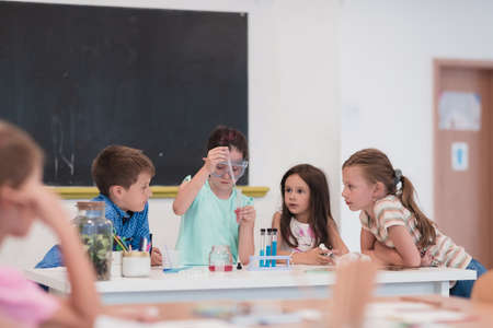 Elementary School Science Classroom: Enthusiastic Teacher Explains Chemistry to Diverse Group of Children, Little Boy Mixes Chemicals in Beakers. Children Learn with Interestの写真素材